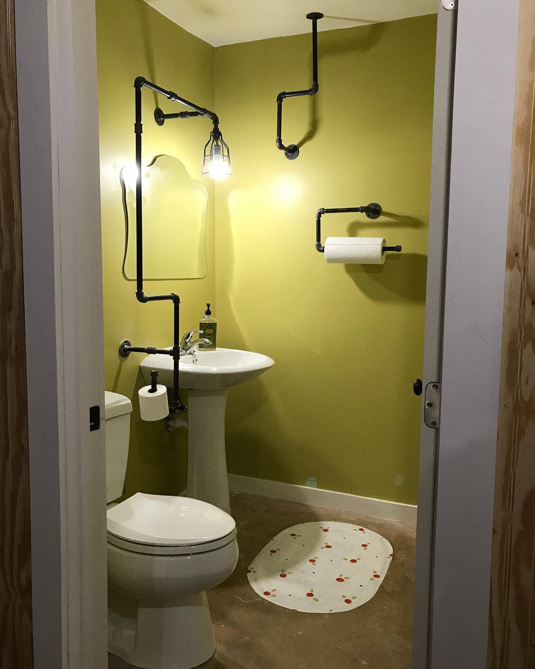 Abstract bathroom with industrial pipe fixtures, pedestal sink, and minimalist green walls.